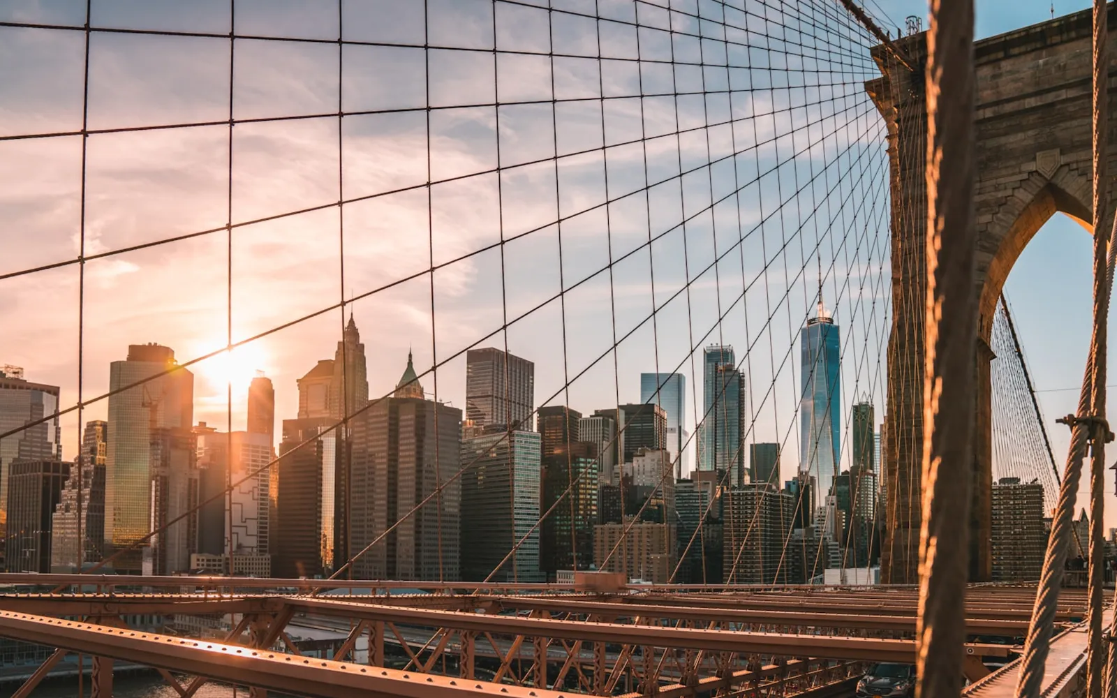 Lower Manhattan skyline at sunset seen through the cables of the Brooklyn Bridge